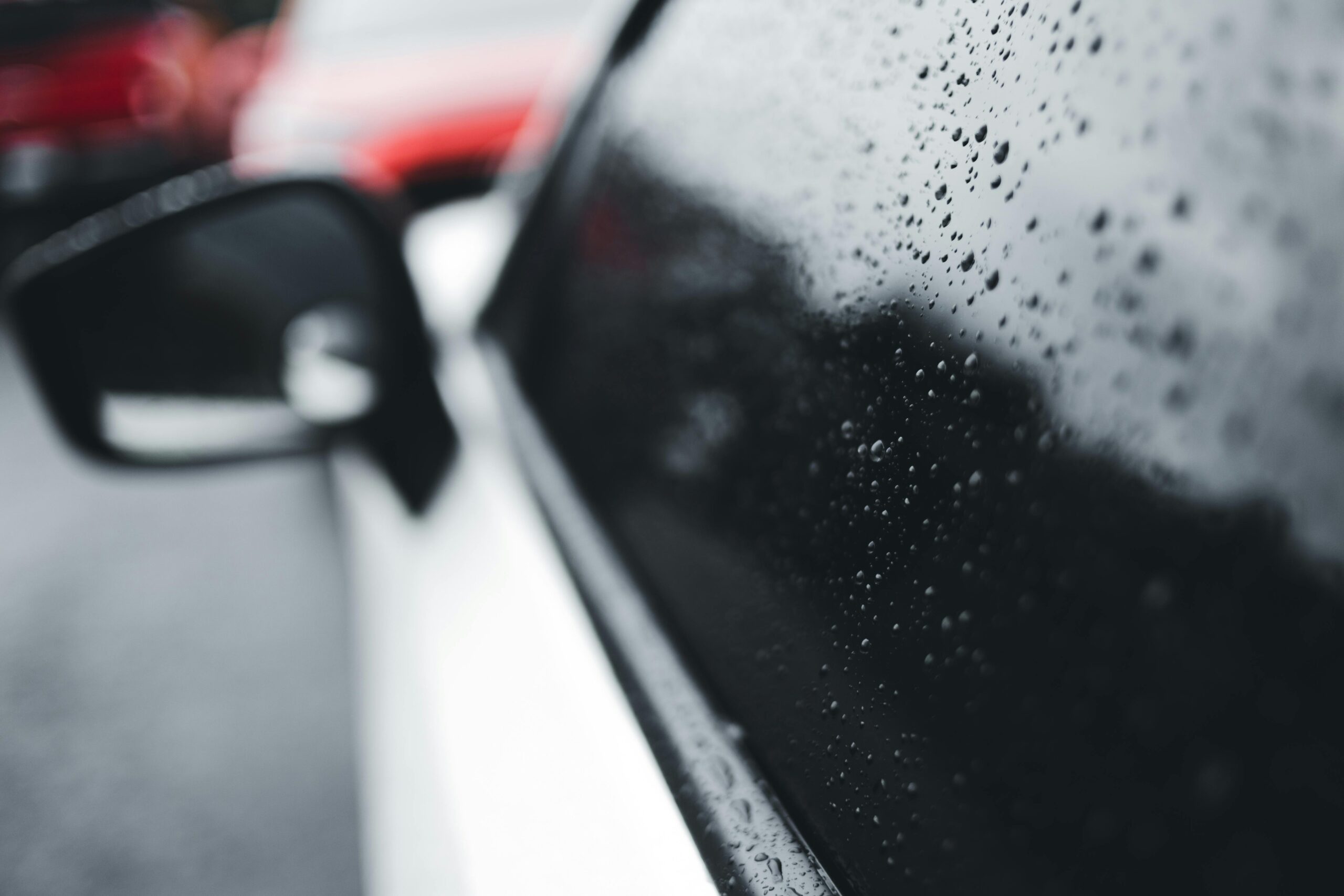 Water droplets on black tinted car windows during rainy weather with blurred side mirror view